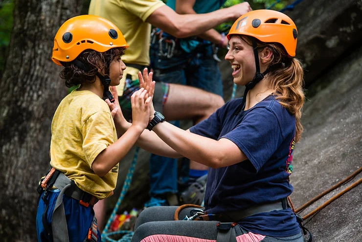 A counselor and a child do activities at camp with a helment for an article about Camp or Wilderness Therapy